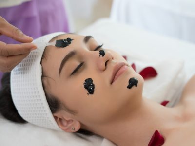 Beautiful woman getting facial black mud mask at beauty salon.