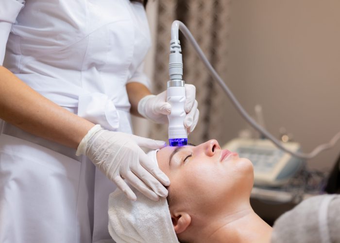 A young beautiful girl lies on the beautician's table and receives procedures with a professional apparatus for skin rejuvenation and moisturizing